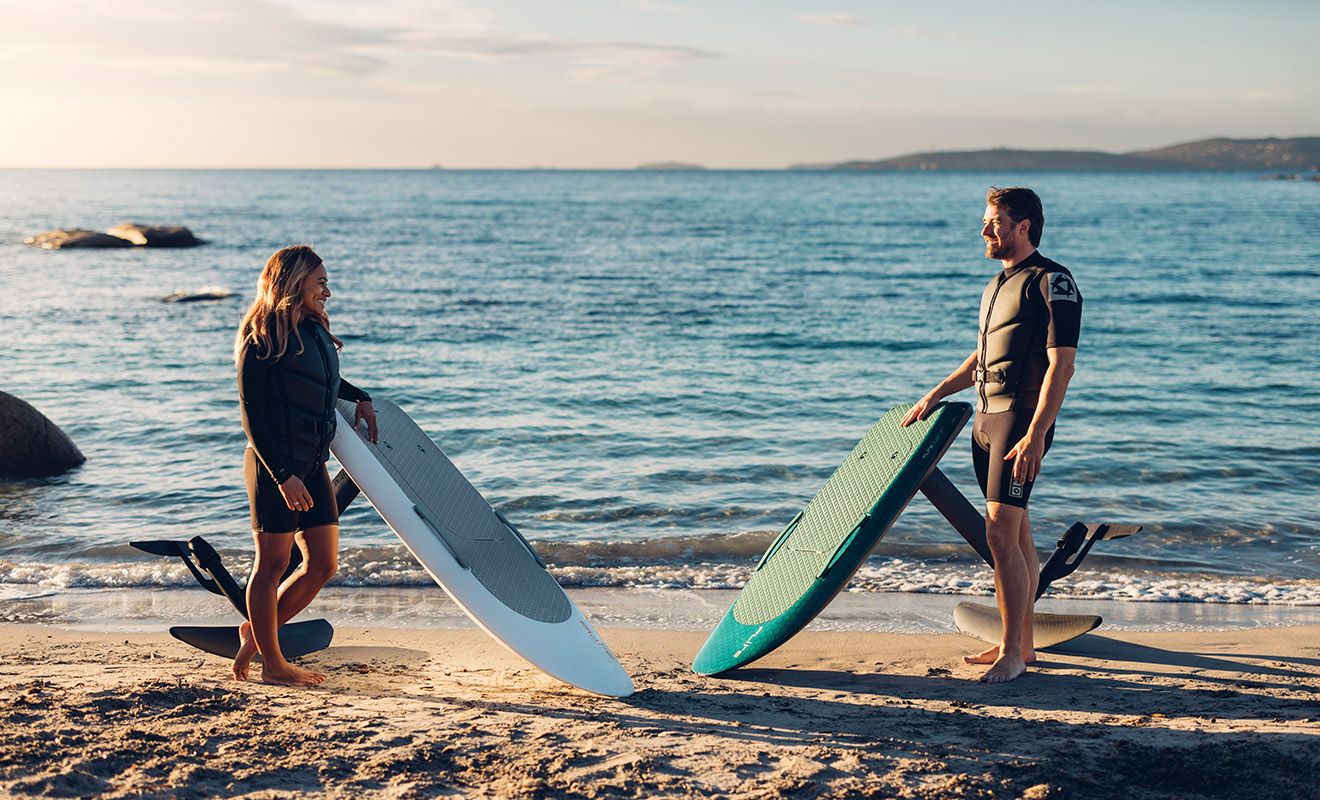 Man and woman standing next to two efoils on the beach 
